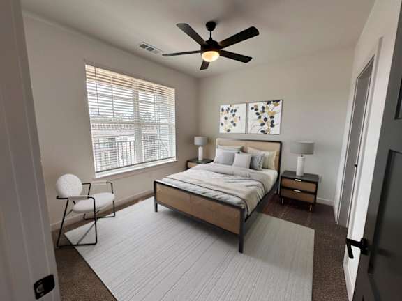 A bedroom with a bed, chair, and ceiling fan.