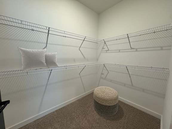 A room with a carpeted stool and wire shelving.