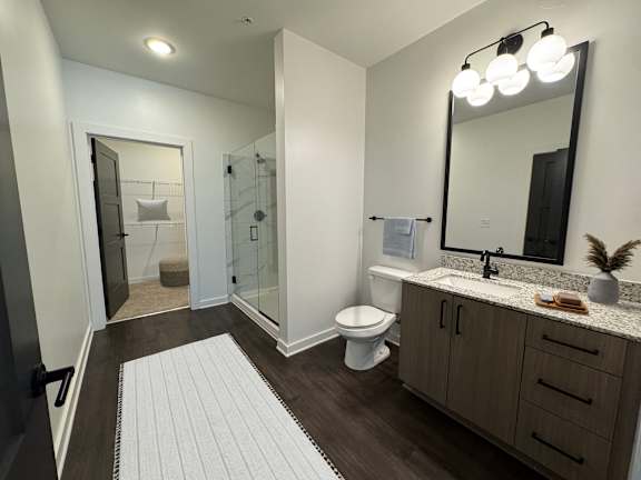 A bathroom with a white toilet, a sink, a mirror, and a glass shower stall.