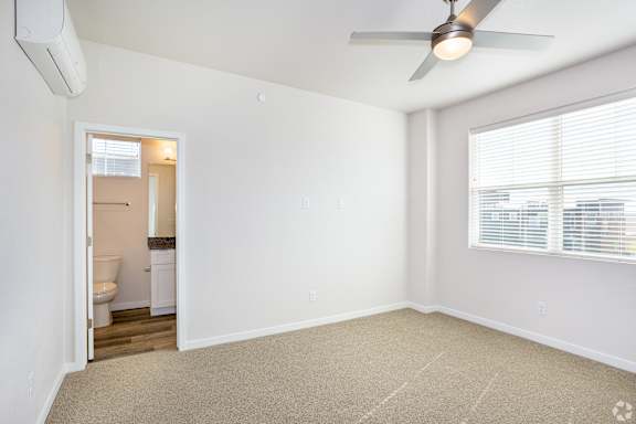 A room with a carpeted floor, a ceiling fan, and a window with blinds.