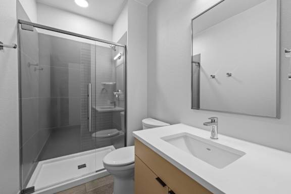 A modern bathroom with a walk-in shower, toilet, and sink at The Avenue Lofts Golden Apartments, Colorado, 80401