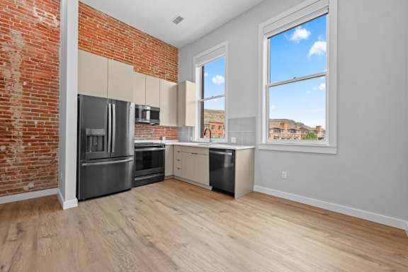 A kitchen with a brick wall and wooden floors at The Avenue Lofts Golden Apartments, Golden, Colorado