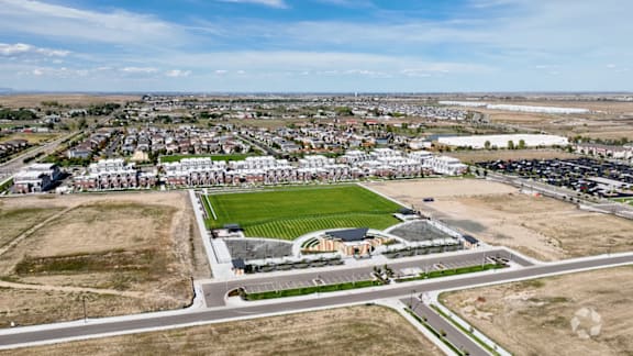 A large open field with a small building and a soccer field in the distance.
