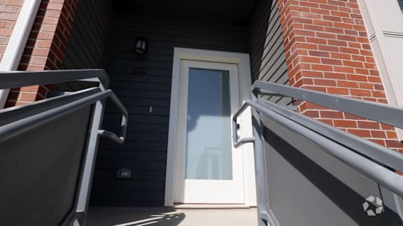 A white door is on the left side of a brick building.
