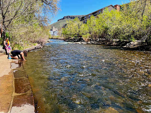 A river flows through a natural landscape with people enjoying the water at The Avenue Lofts Golden Apartments, Colorado, 80401