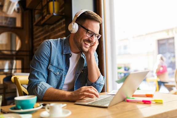 A man in a denim shirt is using a laptop and wearing headphones at The Avenue Lofts Golden Apartments, Golden, Colorado