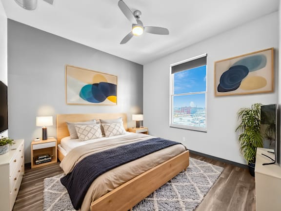 A bedroom with a bed, a ceiling fan, and a window with a view of the city.