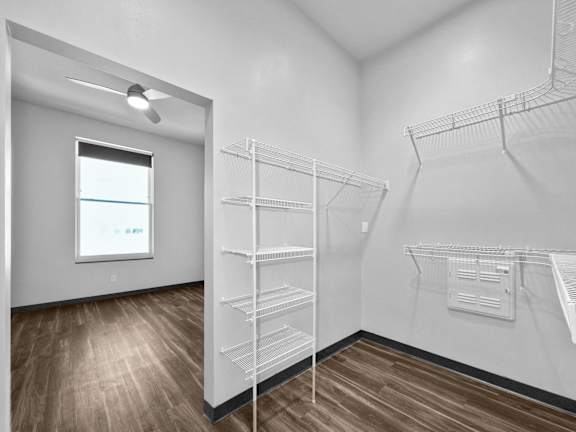 A room with a window and a fan, and a wall with shelves.