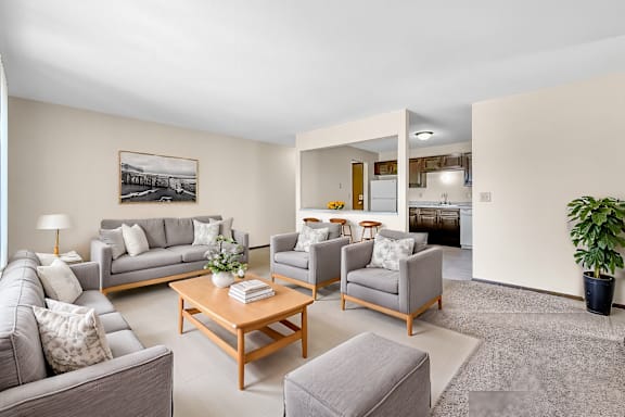A living room with a grey couch, a grey armchair, a grey ottoman, a wooden coffee table, a potted plant, and a framed picture on the wall.