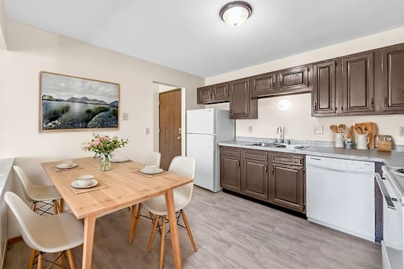 A kitchen with brown cabinets and a wooden table with chairs.