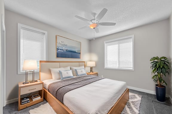 A bedroom with a bed, two lamps, a ceiling fan, and a potted plant.