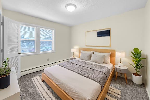 A bedroom with a large bed, a small table with a lamp, and a potted plant.