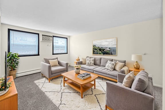 A living room with a grey couch, a grey armchair, a wooden coffee table, and a large window with a view of the ocean.