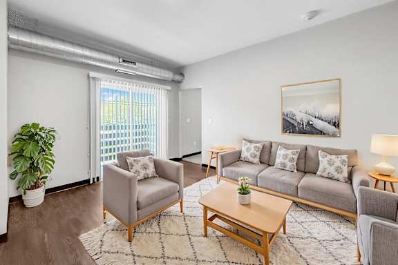 A living room with a grey couch, a wooden coffee table, and a large window with blinds.