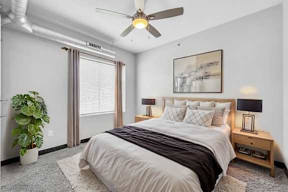 A bedroom with a large bed, a ceiling fan, and a potted plant.