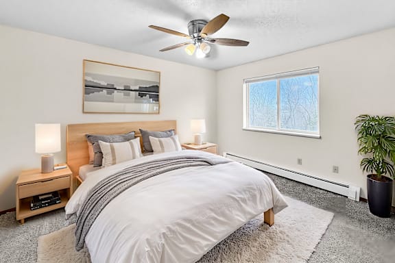 A bedroom with a large bed, a ceiling fan, and a window with blinds.