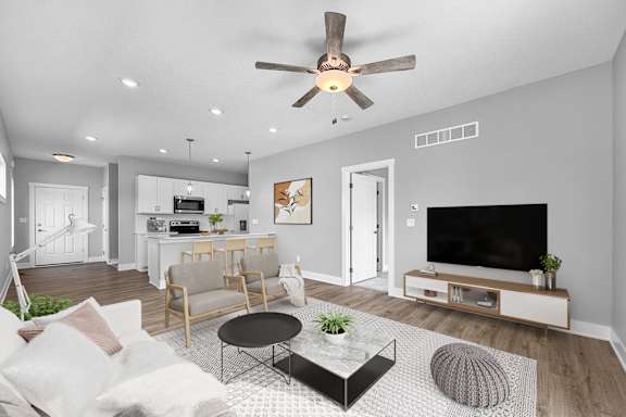 A modern living room with a flat screen TV, a sofa, a coffee table, and a ceiling fan.