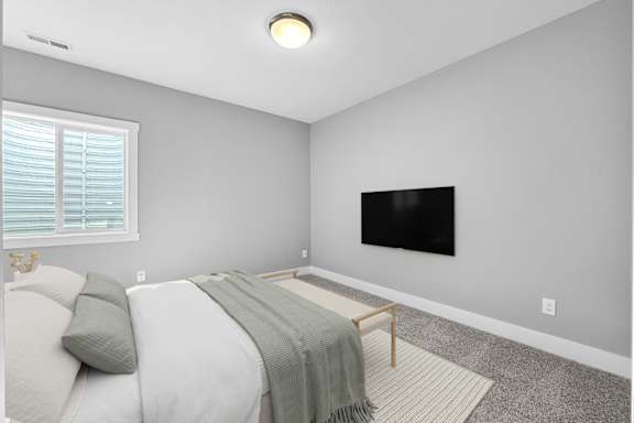 A bedroom with a bed, a blanket, a bench, and a television.