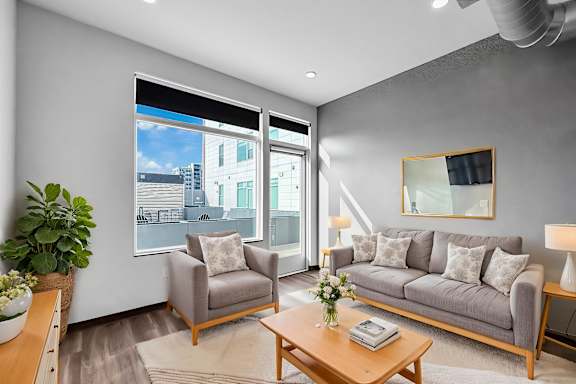 A living room with a grey couch, a wooden coffee table, and a large window with a view of the city.