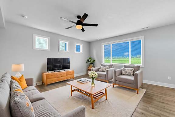 A living room with a grey couch, a wooden coffee table, a flat screen TV, and a ceiling fan.