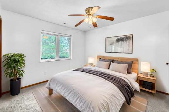 A bedroom with a large bed, a ceiling fan, and a potted plant.