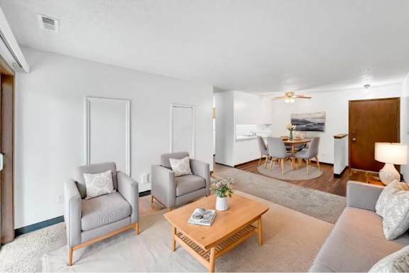 A living room with a grey couch, two armchairs, a coffee table, and a dining area in the background.