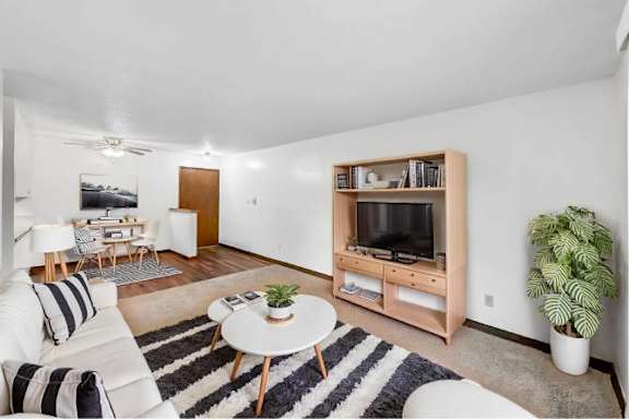 A living room with a white couch, a coffee table, a television, and a potted plant.