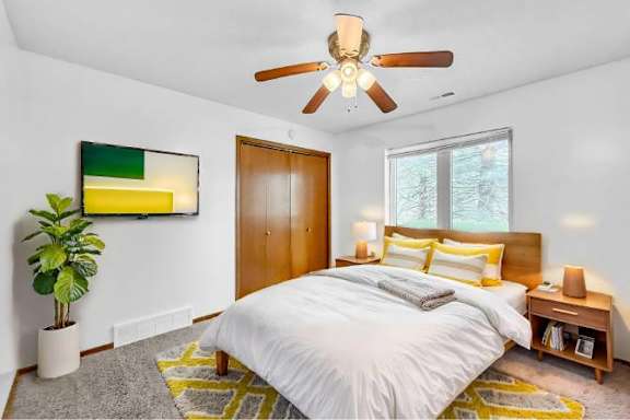 A bedroom with a bed, a ceiling fan, and a potted plant.