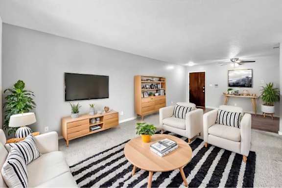 A living room with a black and white striped couch, a wooden coffee table, and a flat screen TV mounted on the wall.