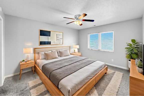 A bedroom with a large bed, a ceiling fan, and a window with blinds.