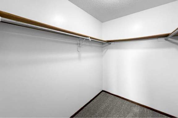 A white wall with a grey carpet and a brown shelf.