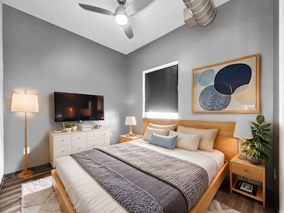 A bedroom with a bed, nightstands, a ceiling fan, and a painting on the wall.