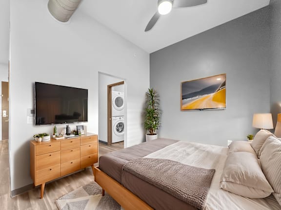 A bedroom with a bed, a dresser, a ceiling fan, and a painting on the wall.
