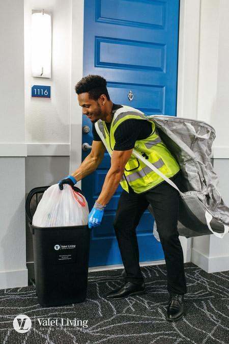 A man in a yellow vest and blue gloves is taking out the trash.