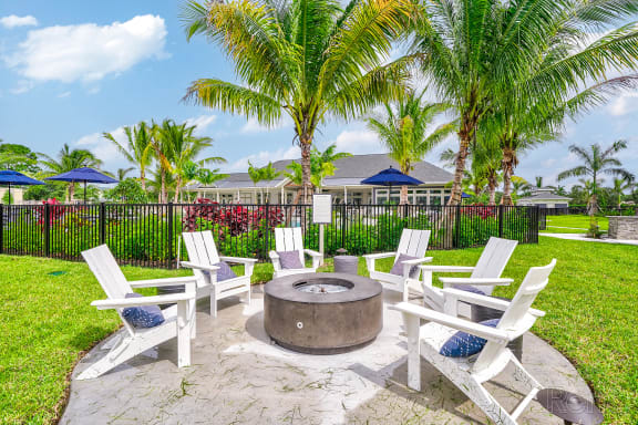 a fire pit with chairs and umbrellas in a grassy area with palm trees