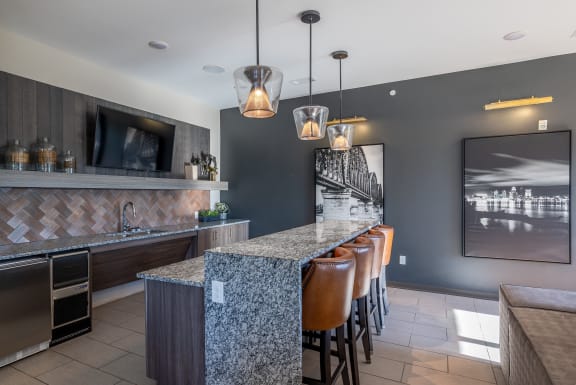 a kitchen with a long bar with chairs and a television