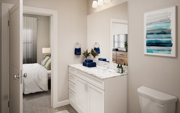a bathroom with a white vanity and toilet and a white bed in the background