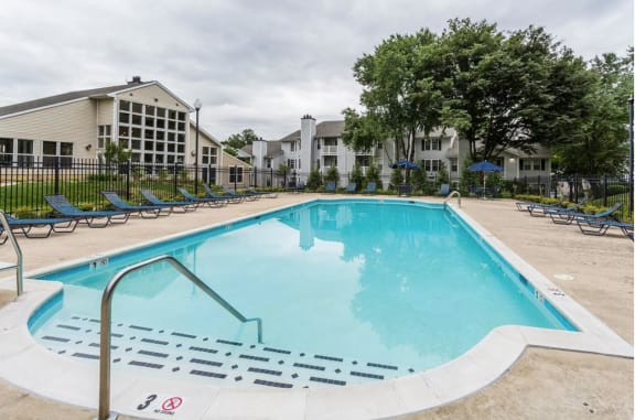 a swimming pool with chaise lounge chairs and apartment buildings in the background at Madison at Eden Brook, Maryland