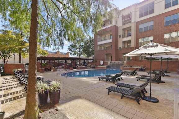 A pool area with sun loungers and a tree.
