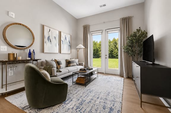 A living room with a grey couch, a round mirror, a coffee table, and a flat screen TV.