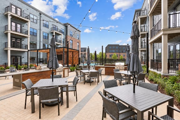 A patio with tables and chairs is surrounded by apartment buildings.