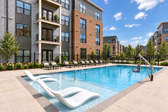 A pool surrounded by lounge chairs in front of apartment buildings.