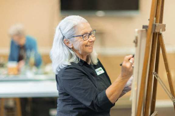 An older woman is painting on a canvas.