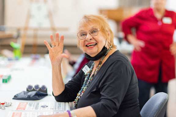 A woman with glasses and a black top is waving her hand.
