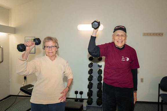 A man and a woman are exercising with dumbbells in a room.