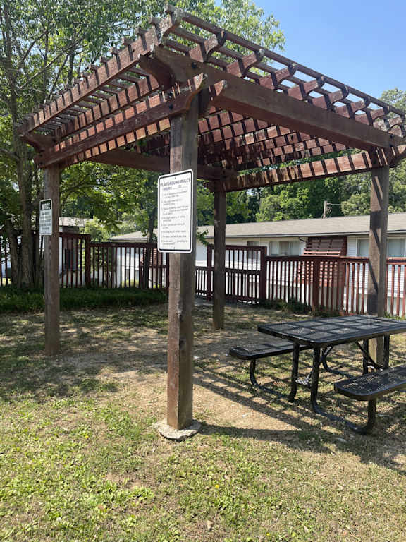 A wooden pergola with a sign and picnic table in the foreground.