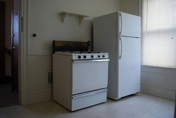 A white refrigerator stands next to a white stove in a kitchen.