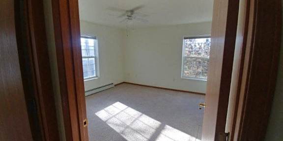 A room with a ceiling fan and two windows.