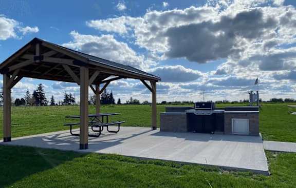 A picnic pavilion with a grill is situated in a grassy field.