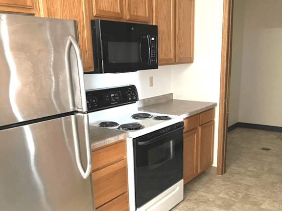 A kitchen with a stainless steel refrigerator, black microwave, and white stove top oven.